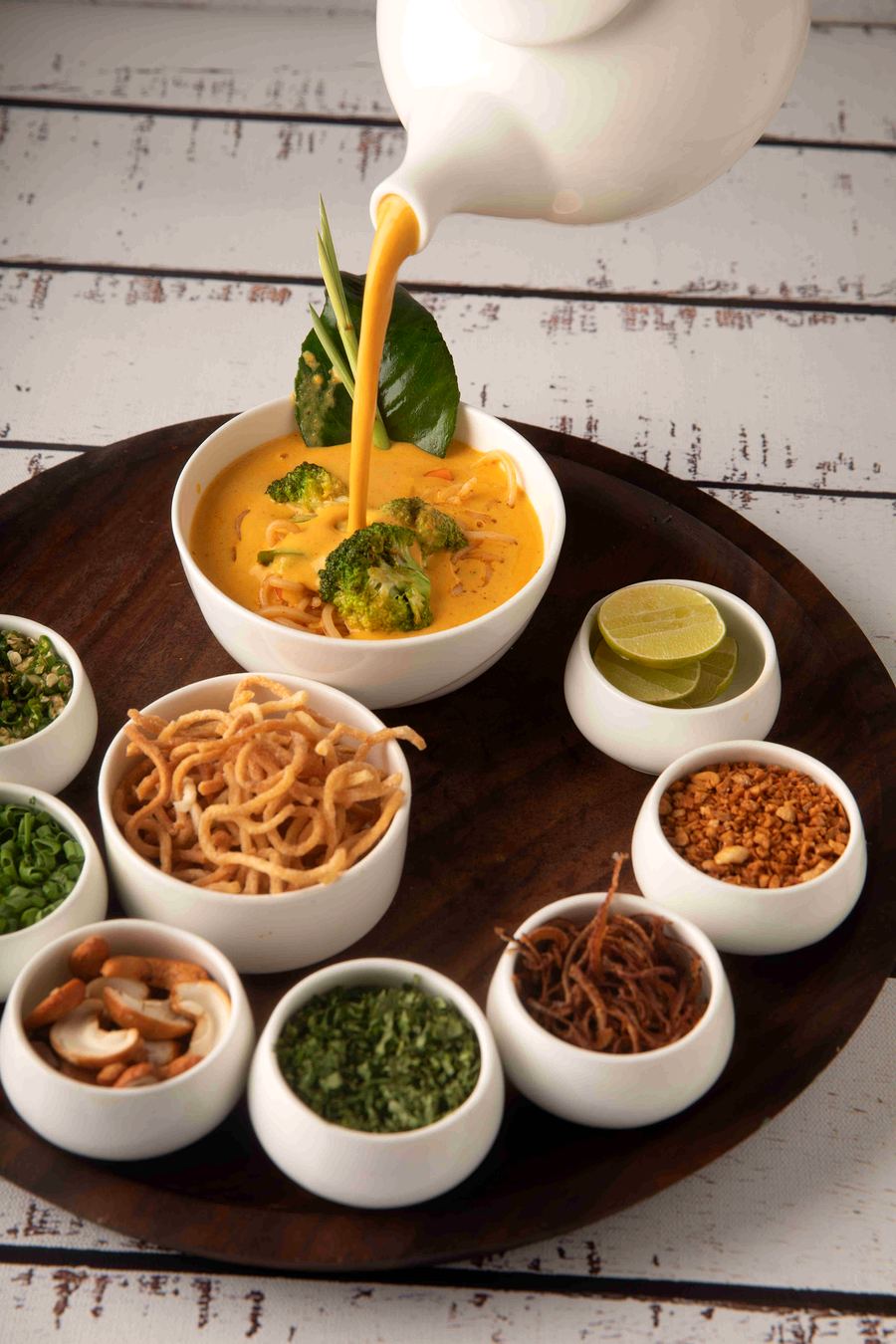 Burmese khao suey being poured tableside with condiments