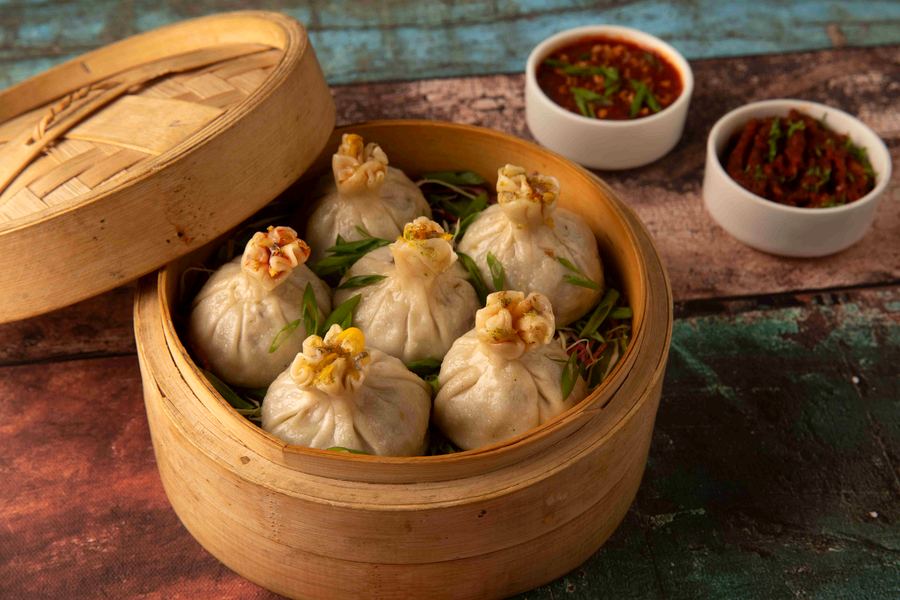 Steamed vegetable momos in a bamboo basket with chutneys